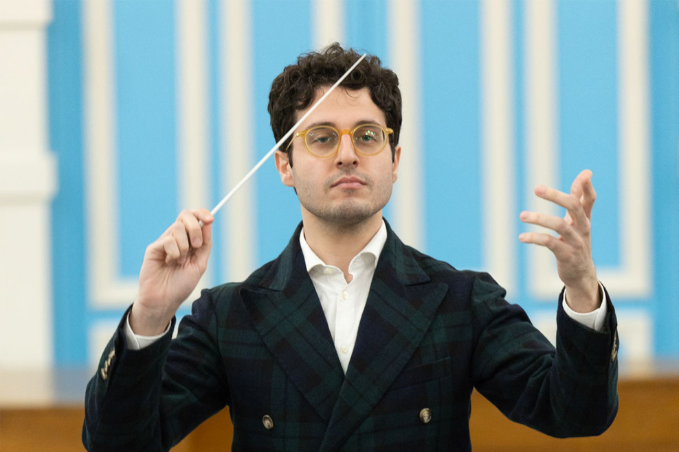 A man wearing a double breasted black jacket, holding a conductor's baton. A man wearing a double breasted black jacket, holding a conductor's baton.